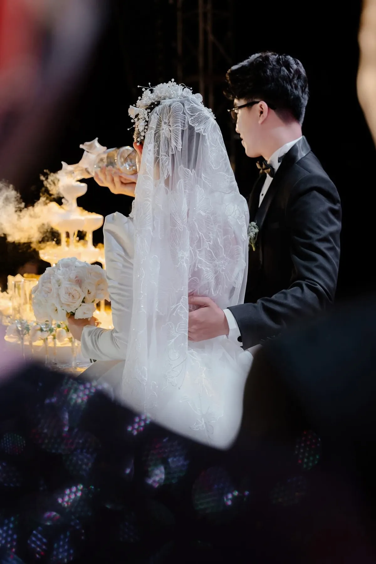 Cô dâu chú rể rót tháp ly, nhìn qua tấm voan